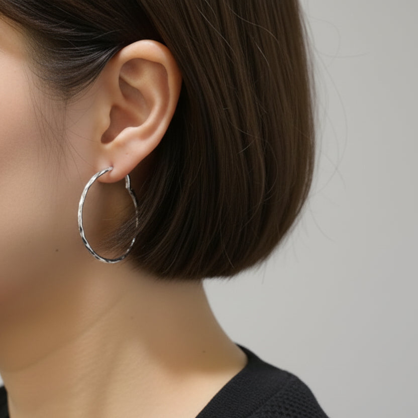 Person wearing a large silver hoop earring with a blurred indoor background