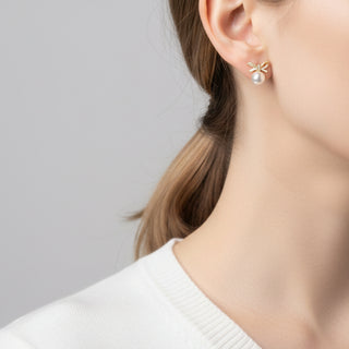 Elegant gold bow stud earrings with white pearls & cubic zirconia. Lightweight, playful design. Perfect for everyday charm & special occasions.