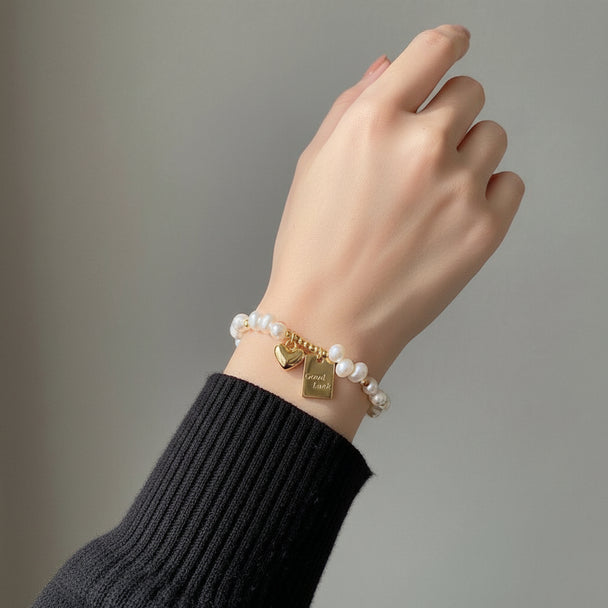 Freshwater pearl bracelet with gold Good Luck & heart charms. Adjustable fit, stackable design. Perfect gift for everyday elegance & positive vibes.