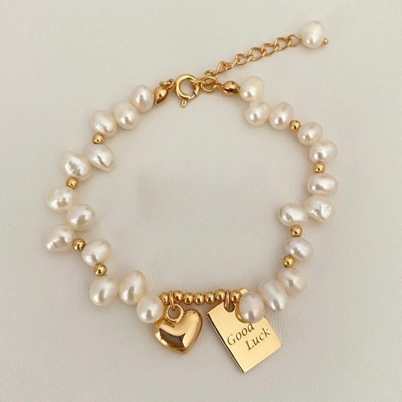 Freshwater pearl bracelet with gold Good Luck & heart charms. Adjustable fit, stackable design. Perfect gift for everyday elegance & positive vibes.