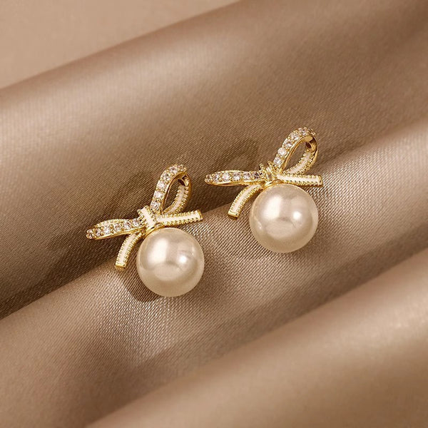 Elegant gold bow stud earrings with white pearls & cubic zirconia. Lightweight, playful design. Perfect for everyday charm & special occasions.